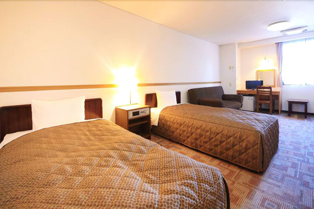 Una habitación de hotel con dos camas, un escritorio, una silla y una mesita.