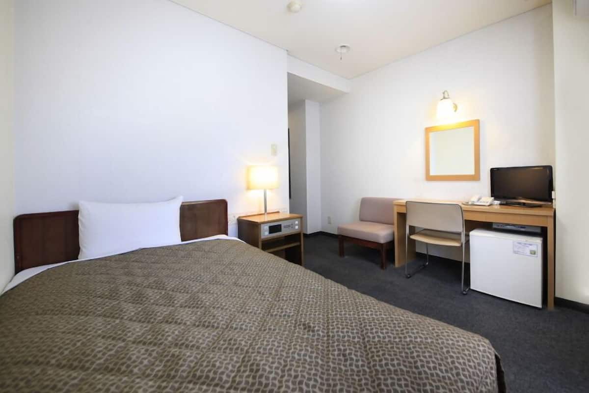 Una habitación de hotel con cama, escritorio, silla y un refrigerador pequeño.