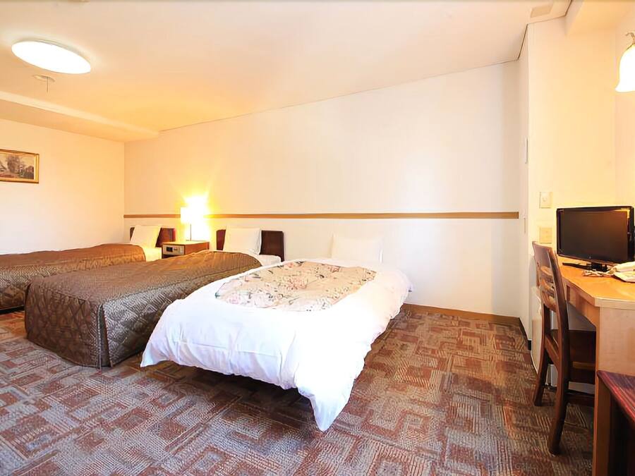 A hotel room with two beds, a desk with a computer, a chair, a lamp, and a television.