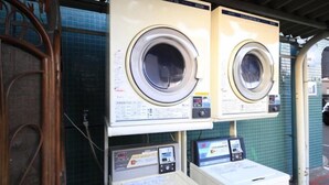 Two front-loading washing machines with control panels, a metal door, and a tiled wall in the background.