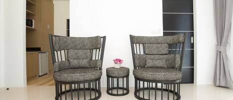 Dos sillones con un reposapiés redondo en una habitación moderna, con una cocina al fondo.