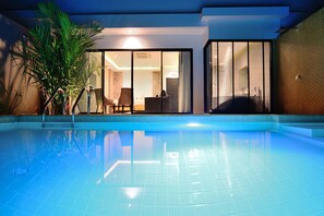 A modern indoor swimming pool with clear blue water, a seating area with chairs, and a large potted plant. - Pumeria Resort Phuket (Choeng Thale)