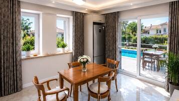 Un comedor moderno con una mesa y sillas de madera, ventanas amplias y vistas a una piscina.