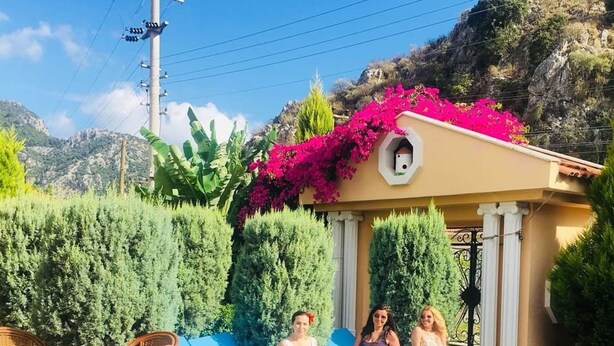 Un espace aménagé au bord de la piscine, avec des chaises longues, une table à manger et un bâtiment doté d’un balcon.