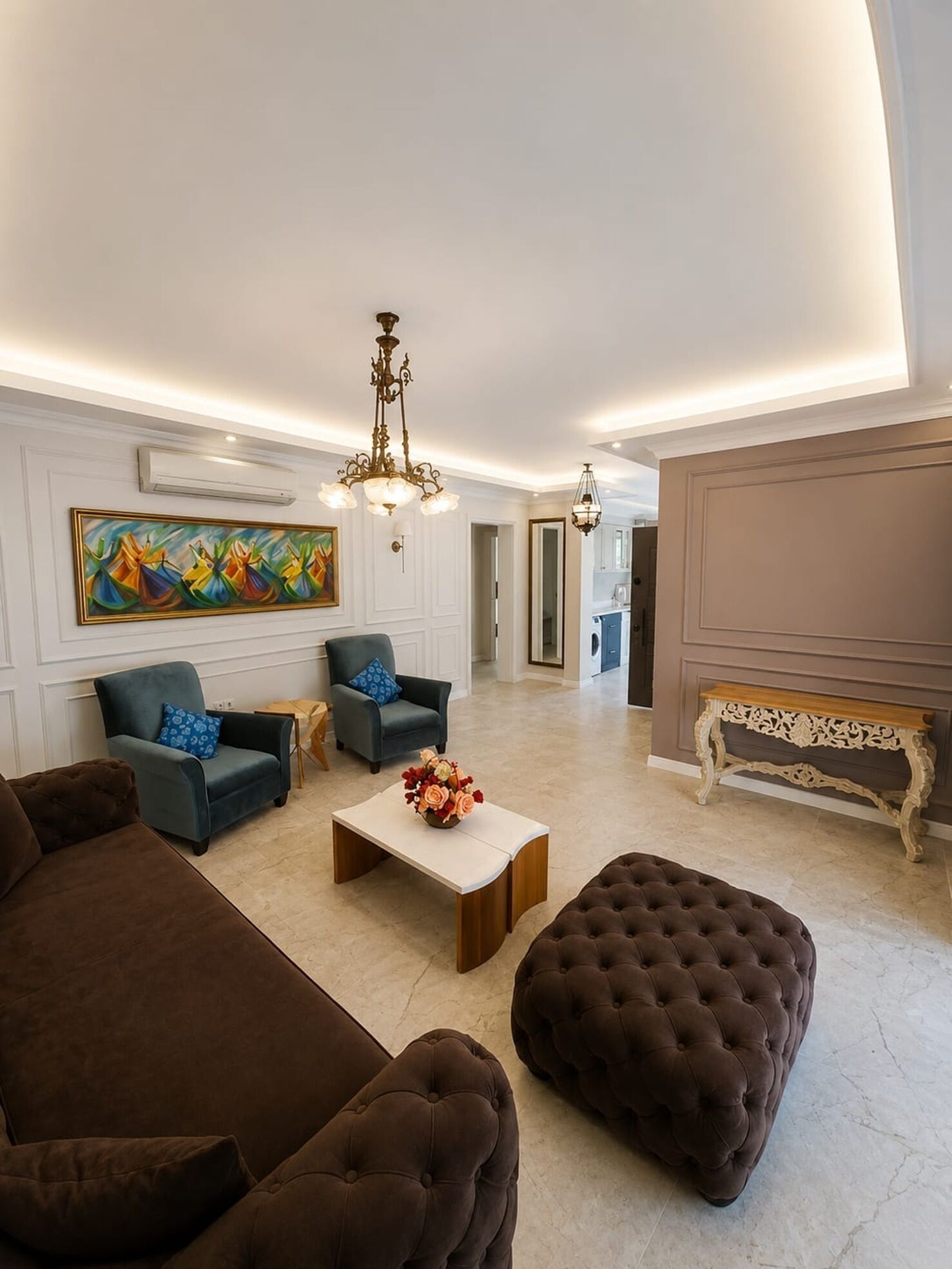A spacious living room with a large sofa, a coffee table with a floral centerpiece, and a chandelier.