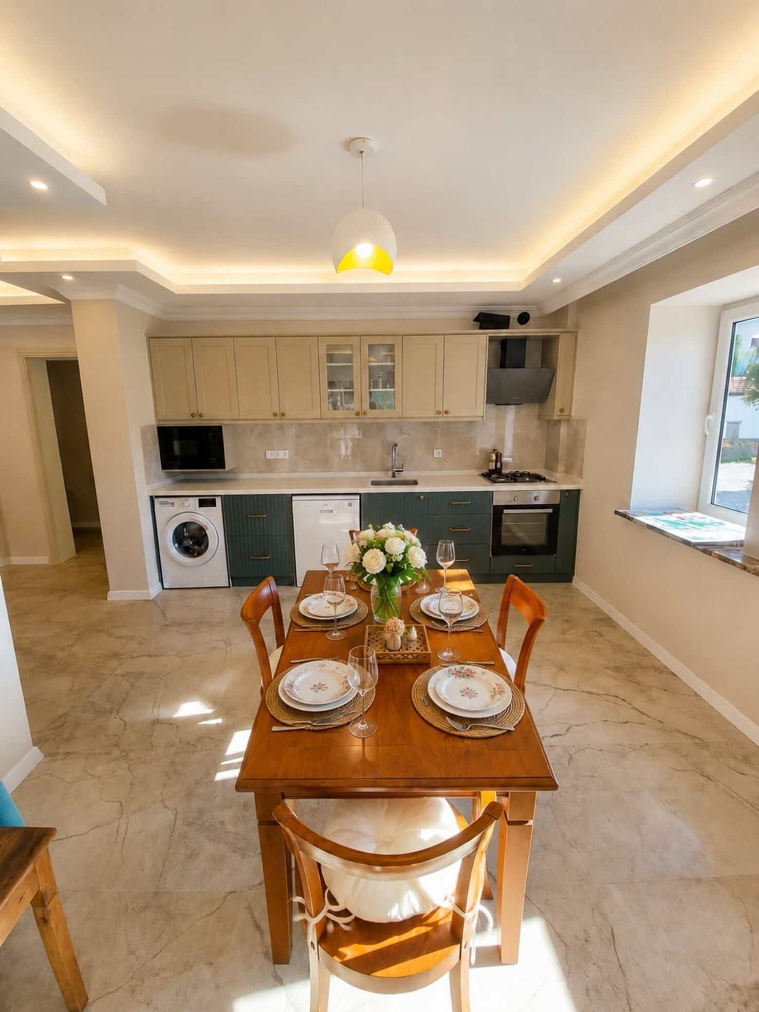 A modern kitchen with built-in appliances, a dining area with a wooden table set for four, and a view of the outdoors through a window.