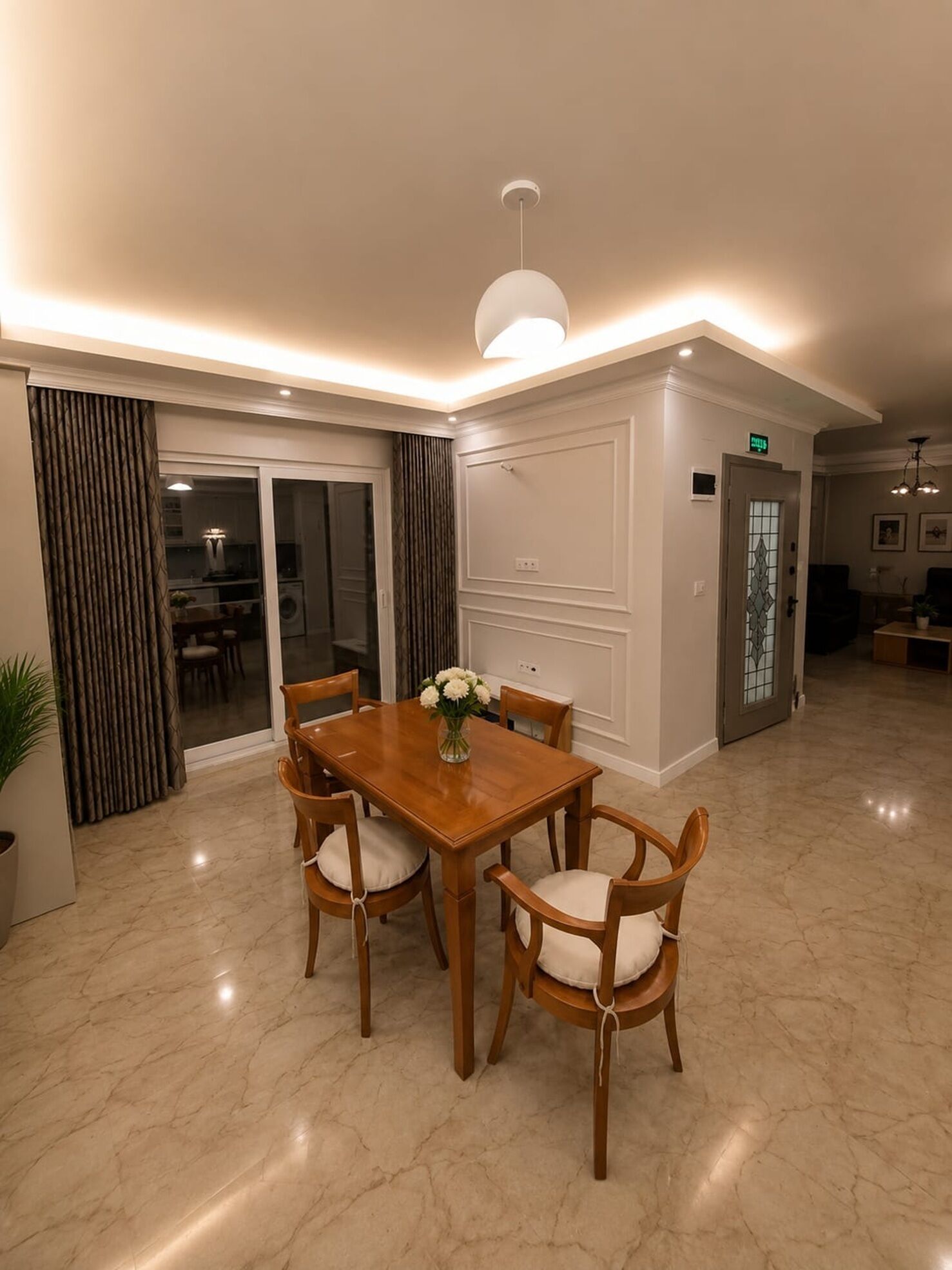 A dining area with a wooden table and chairs, a vase with flowers, and a modern pendant light.