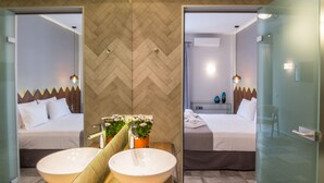 Una habitación de hotel moderna con un espejo grande, dos lavabos, una cama y una mesita con un jarrón de flores.