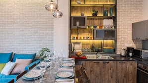 Una cocina moderna con pared de ladrillo, armarios de madera y comedor con sofá azul y mesa preparada para cuatro.