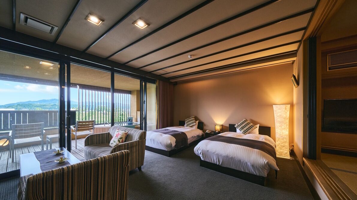 Ein Hotelzimmer mit zwei Betten, einem Balkon mit Blick und einer Essecke mit Tisch und Stühlen.