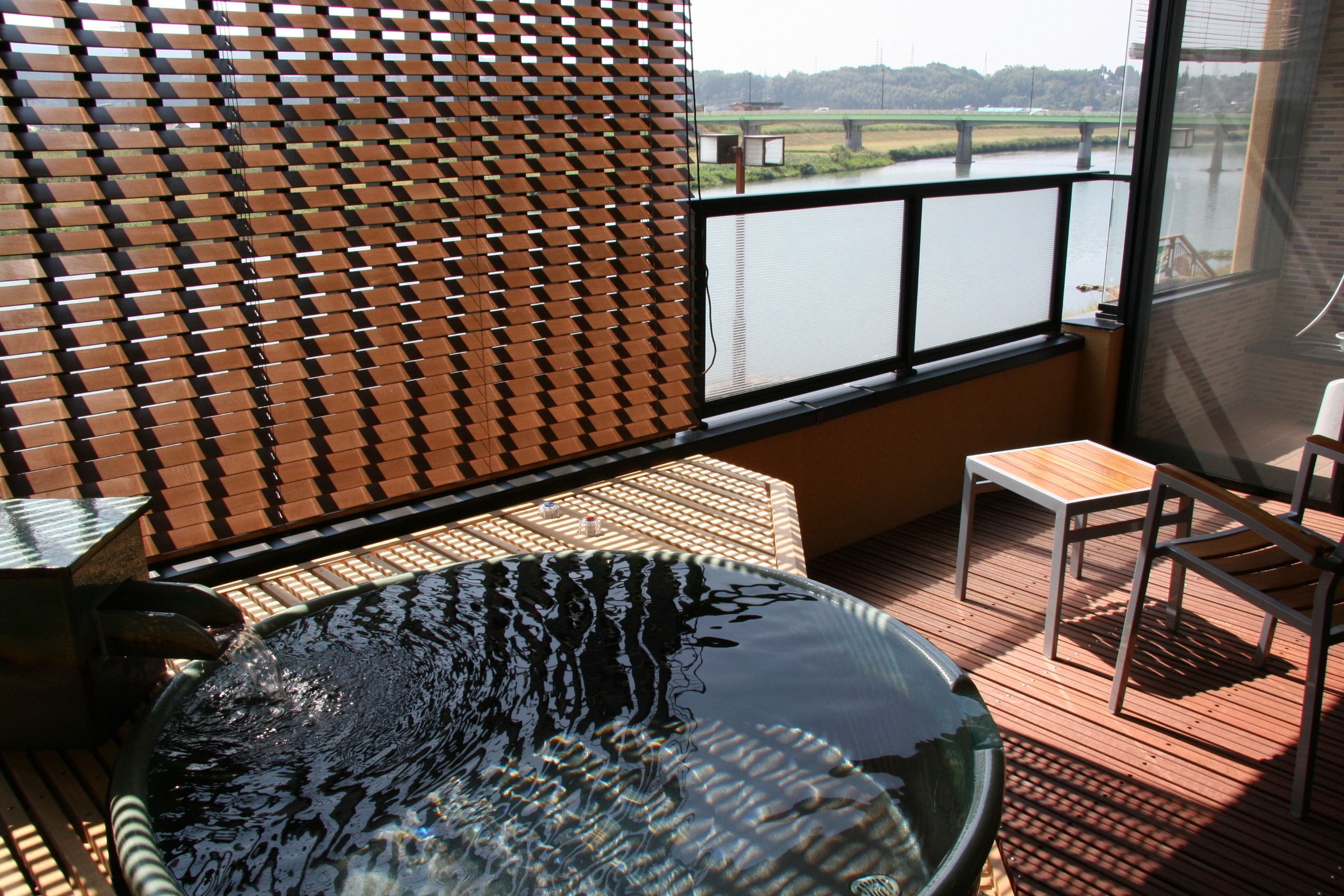 A deck with a glass-bottomed hot tub, a wooden table, and a chair.