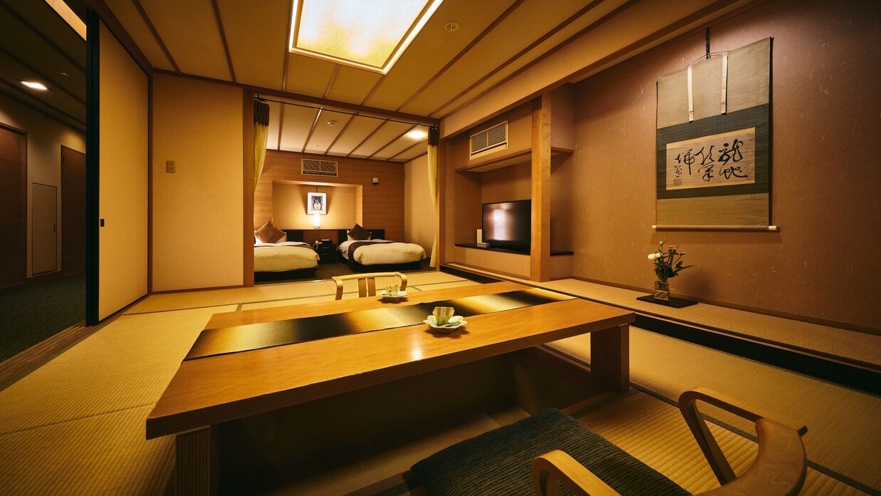 Ein traditioneller japanischer Raum mit Tatami-Böden, einem niedrigen Tisch, Betten mit Futon-Matratzen und einem Fernseher.