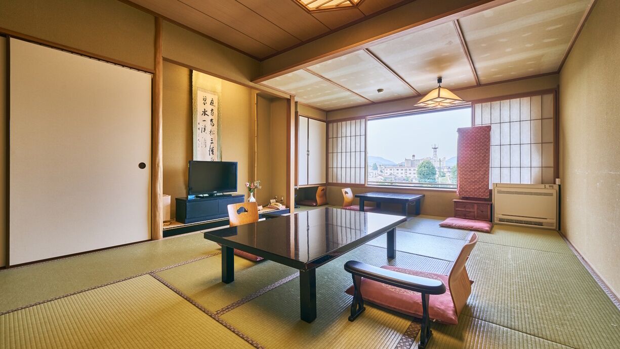 Una habitación tradicional japonesa con suelo de tatami, una mesita baja, cojines, un televisor y vistas a la ciudad.