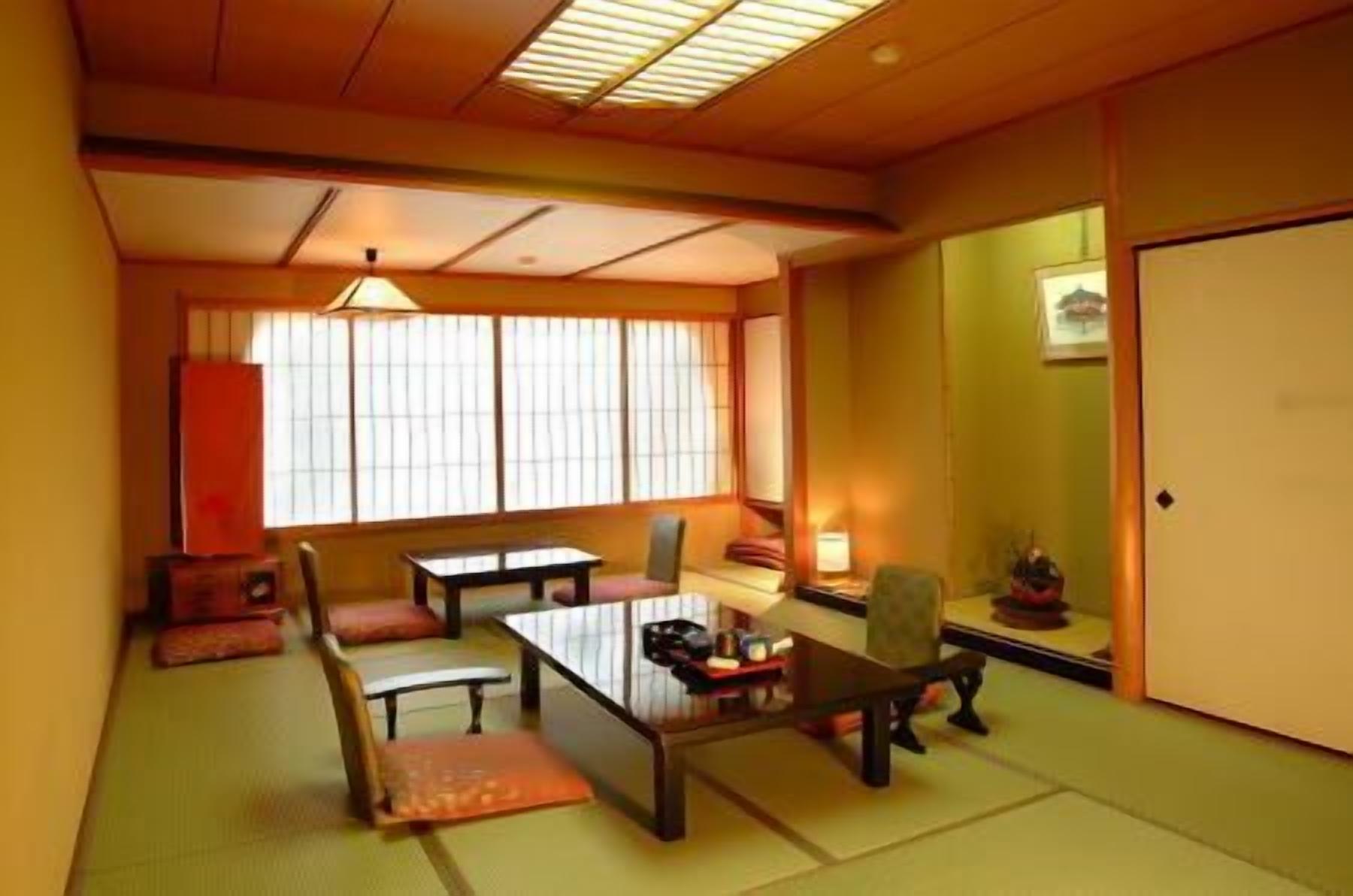 Una habitación de estilo japonés tradicional con suelo de tatami, una mesa baja, sillas y un puertas correderas.
