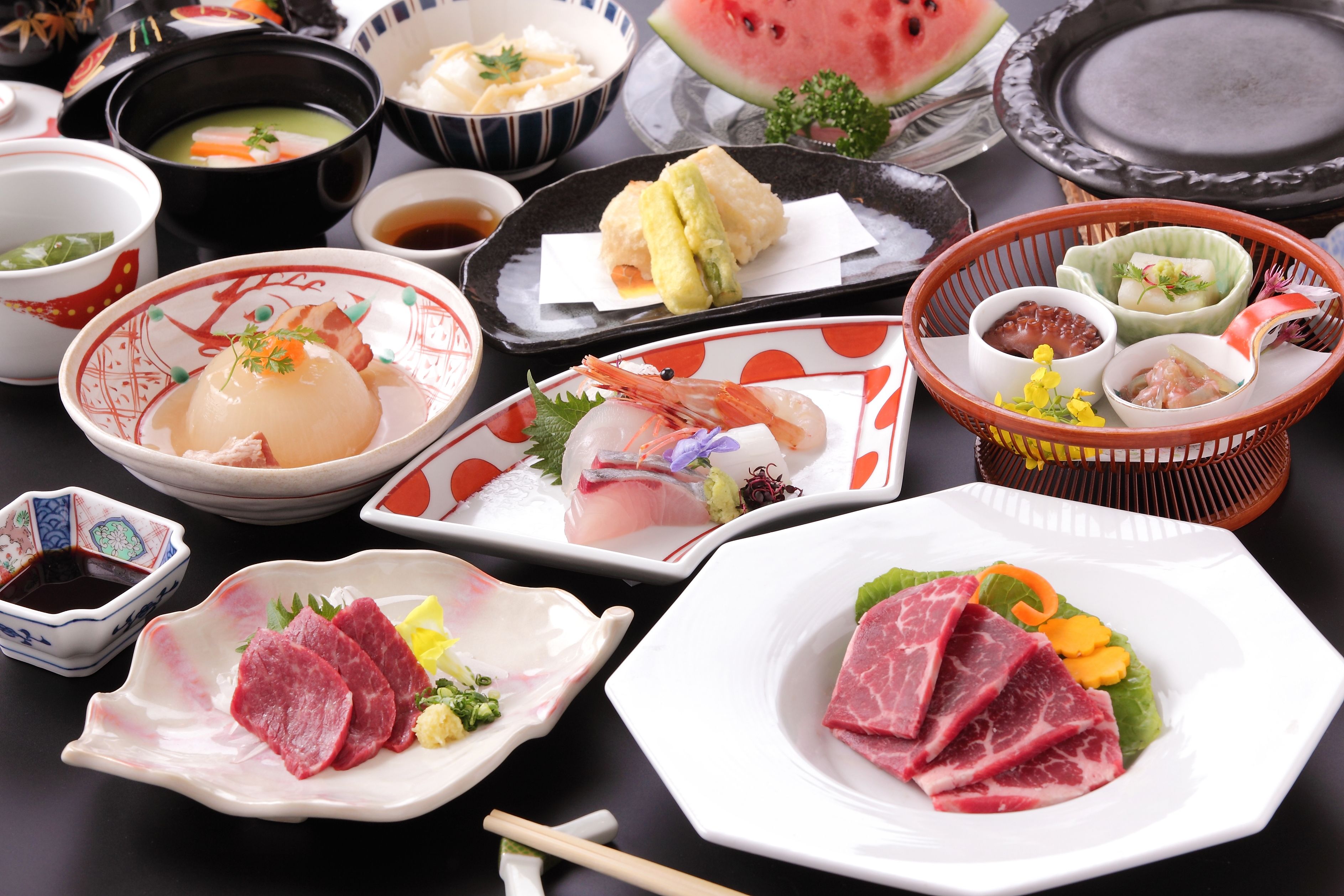 A variety of dishes including sashimi, vegetables, and a watermelon.