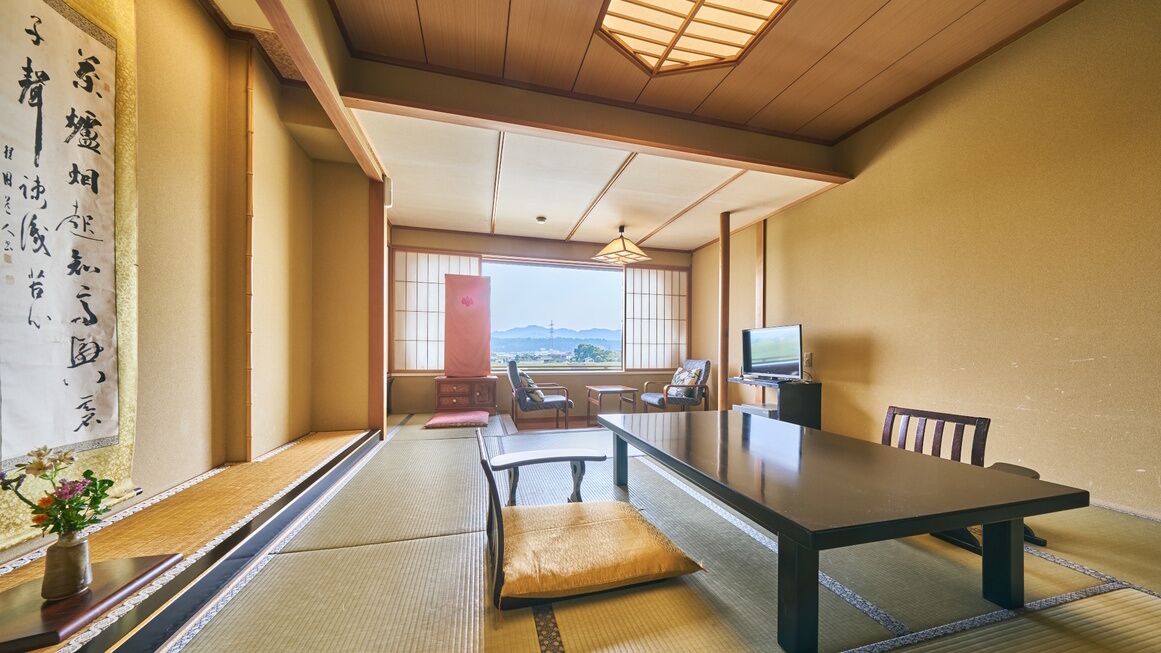 Una habitación japonesa tradicional con suelo de tatami, una mesa baja, sillas, un televisor y vistas al exterior.