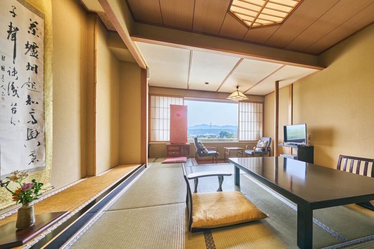 A traditional Japanese room with tatami flooring, a low table, chairs, a television, and a view of the outdoors.