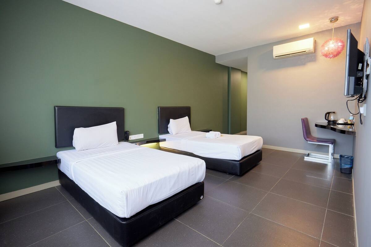 Une chambre d’hôtel avec deux lits, un téléviseur à écran plat, un système de climatisation et un petit bureau avec une chaise.