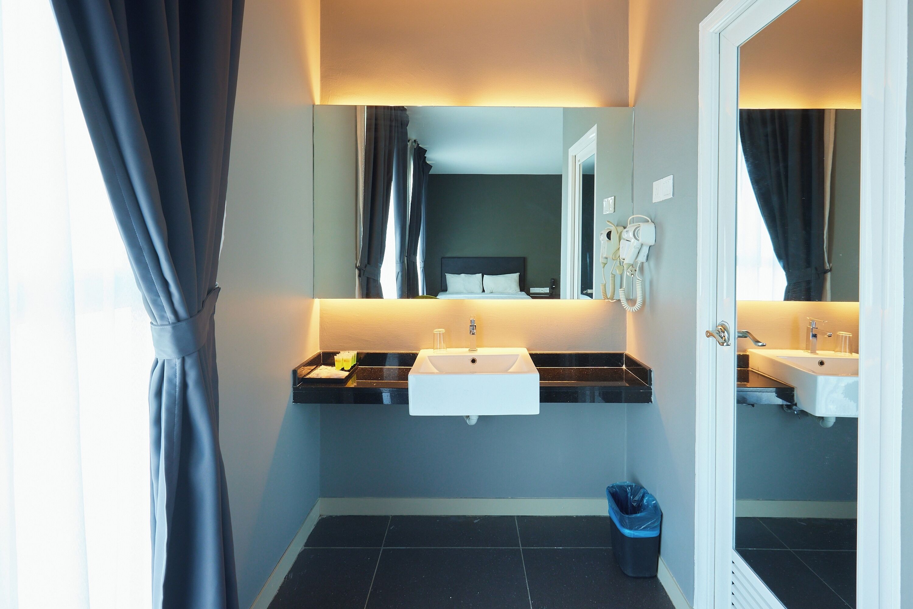 A modern bathroom with two sinks, a mirror, and a trash bin.