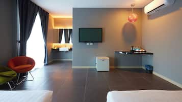 A hotel room with a bed, a TV, a small kitchenette, a chair, and a trash bin.