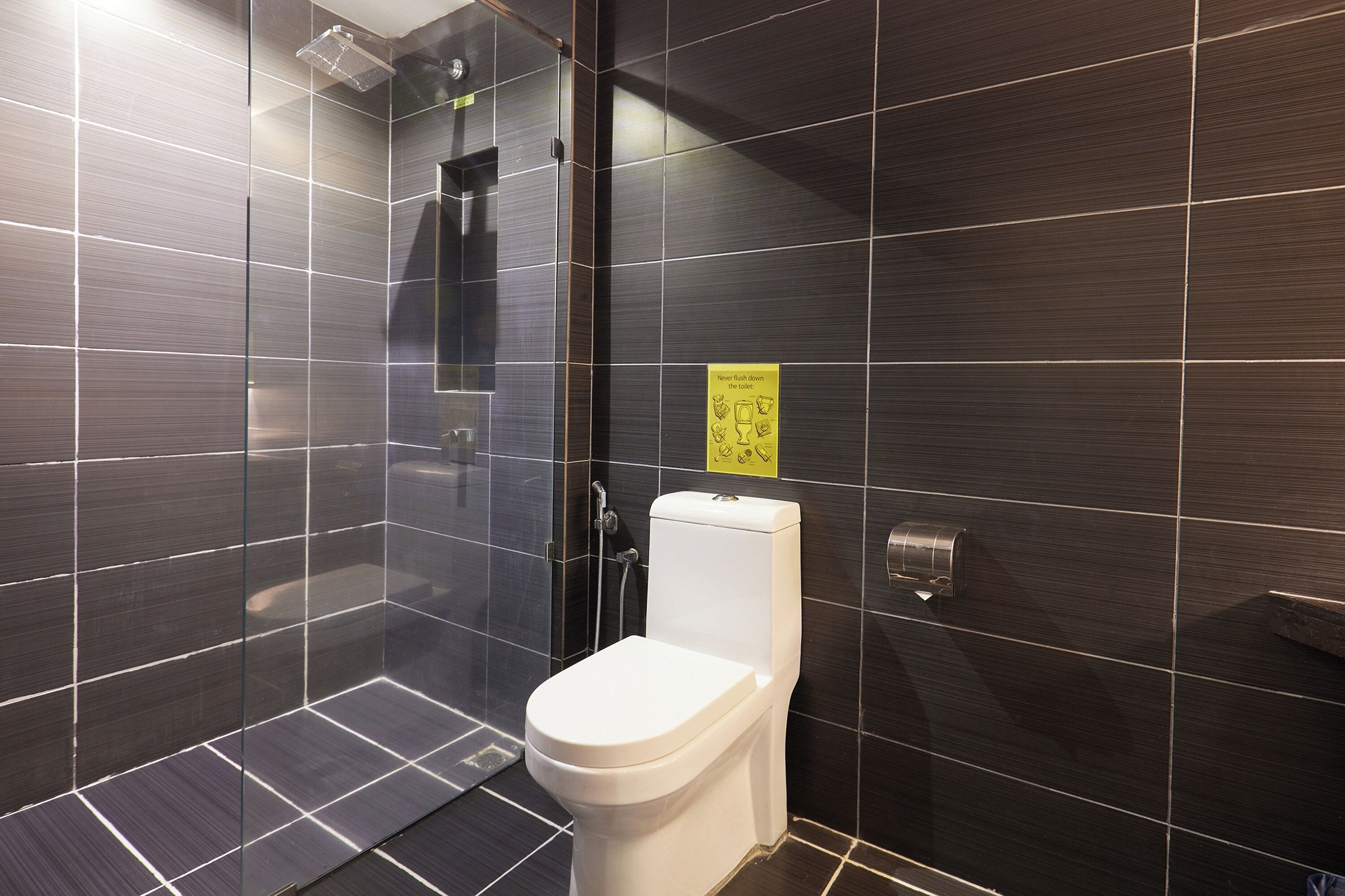 Et moderne badeværelse med mørke fliser, en glasafskærmet brusekabine og et toilet.
