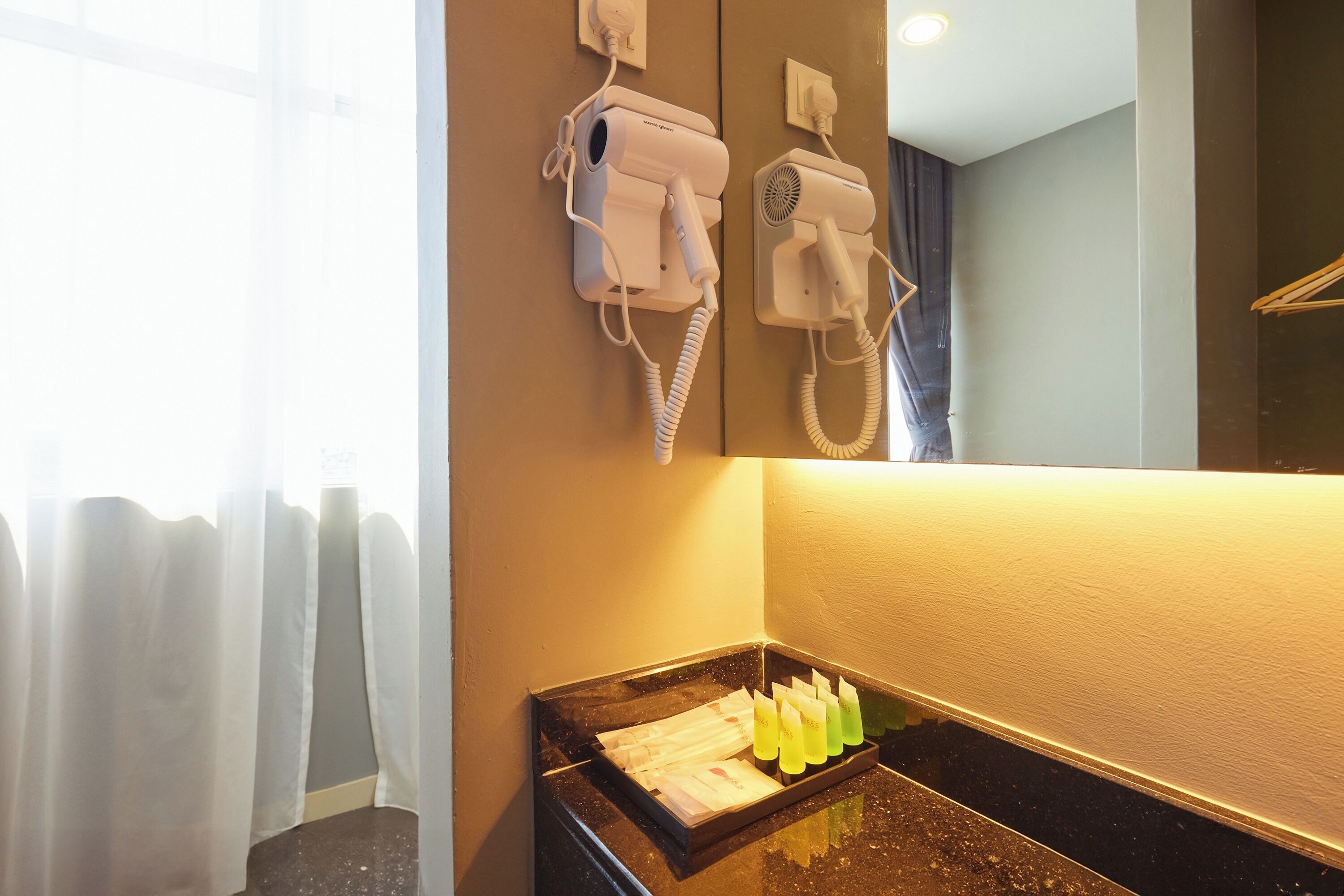 Une salle de bain équipée d’un sèche-cheveux et d’un téléphone mural, d’un lavabo avec un miroir et d’un porte-serviettes.