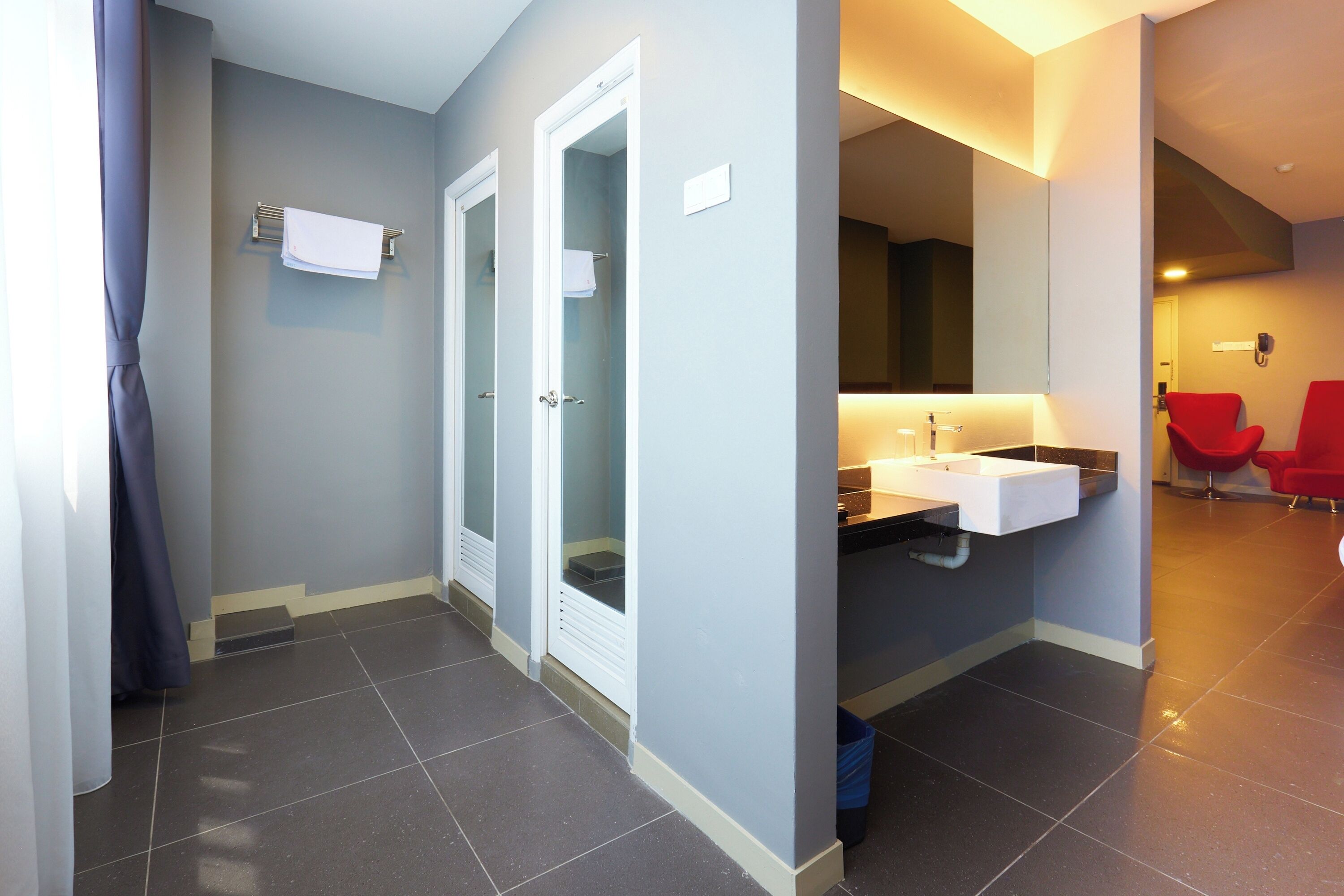 A modern bathroom with a large mirror, a white sink, and two red chairs.