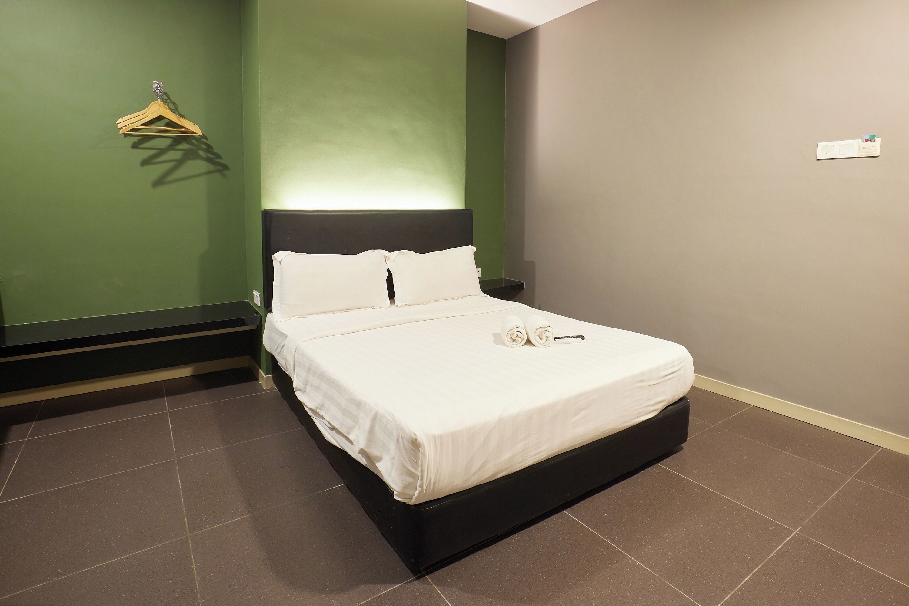 Una cama bien hecha con sábanas blancas y un cabecero negro en una habitación con paredes verdes y grises.
