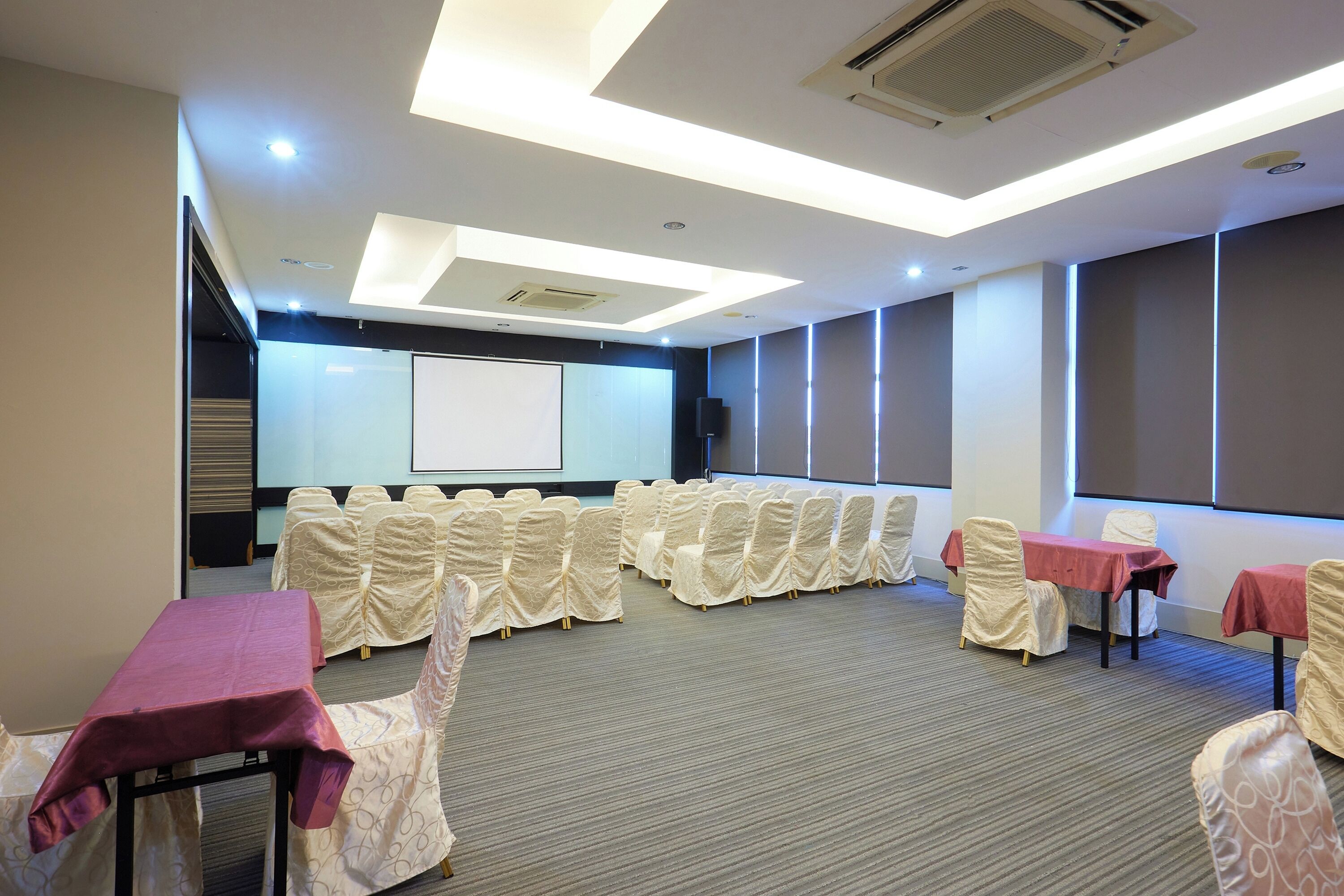A conference room with rows of chairs, tables with red tablecloths, and a projector screen.