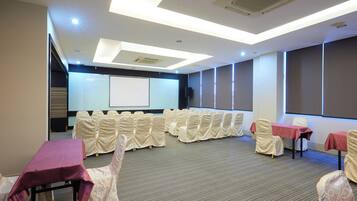 A conference room with rows of chairs, tables with red tablecloths, and a projector screen.