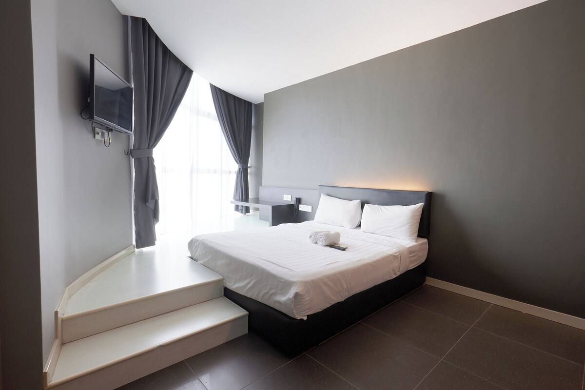 Une chambre d’hôtel moderne, équipée d’un lit, d’un téléviseur fixé au mur et d’un escalier menant à un étage supérieur.