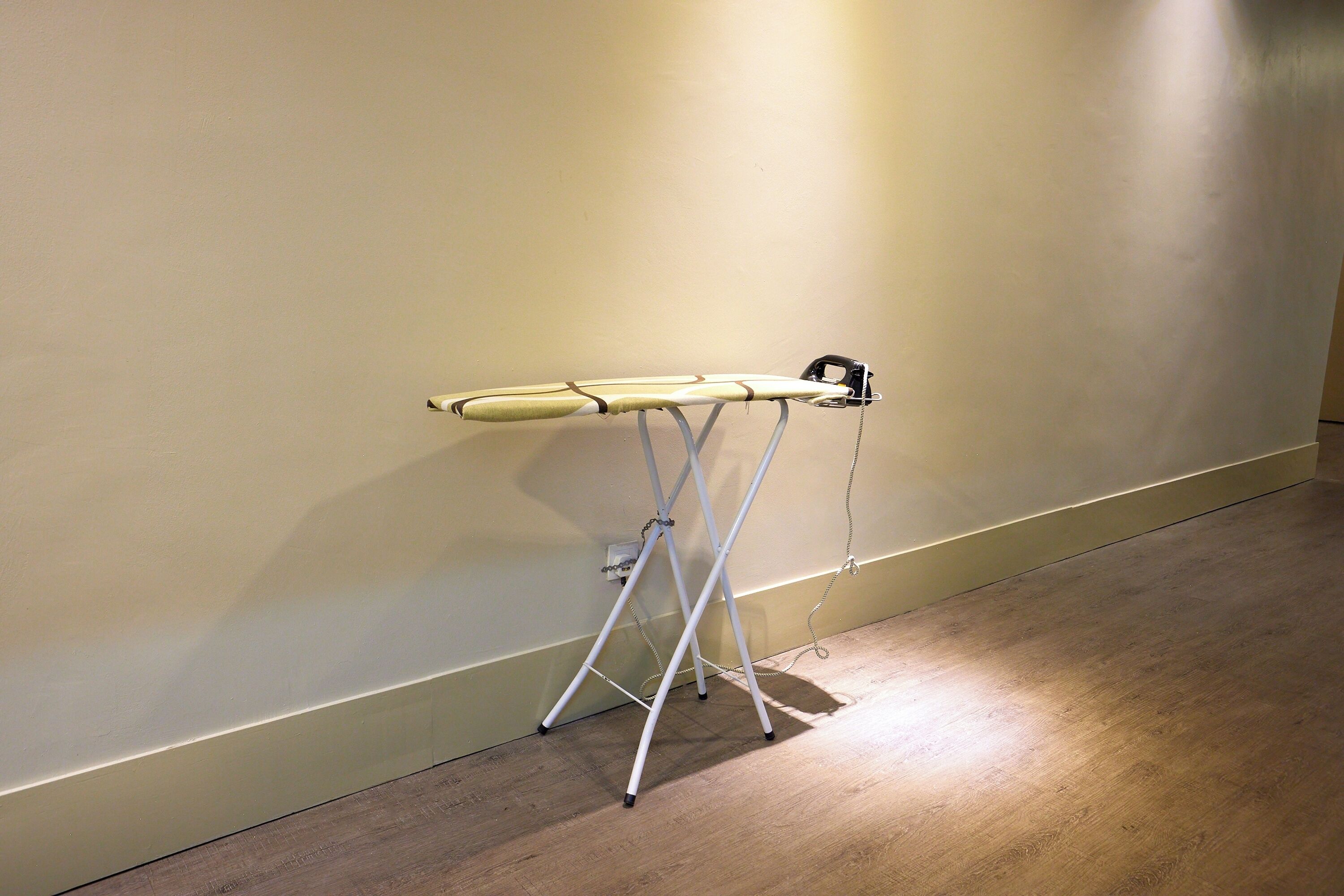A room with a wooden floor and a white ironing board against a plain wall.