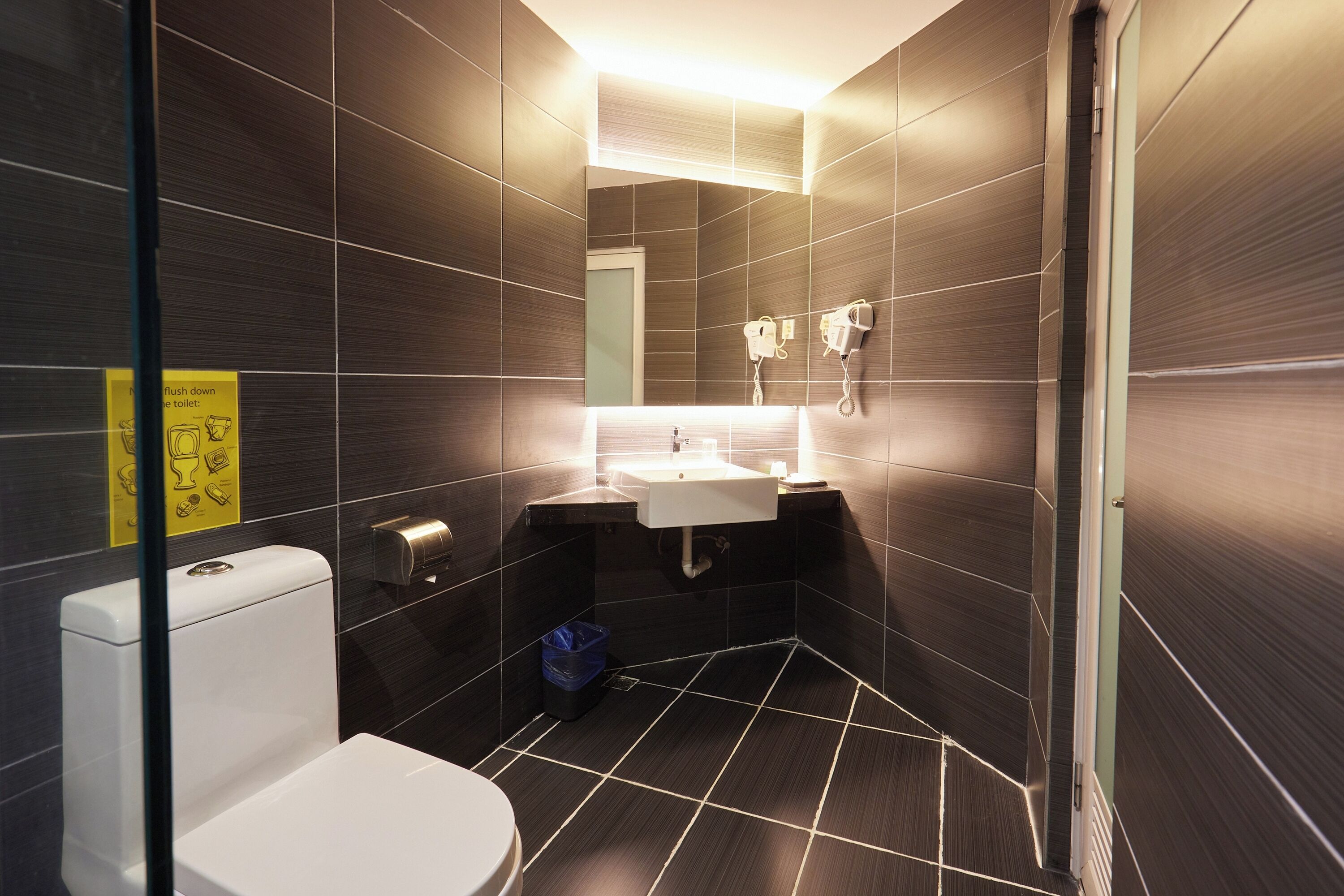 A modern bathroom with dark tiles, a white toilet, a sink, and a mirror.