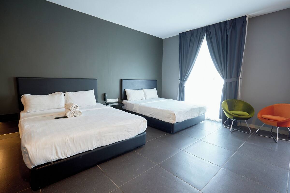 Une chambre d’hôtel avec deux lits, une grande fenêtre avec des rideaux et deux chaises.