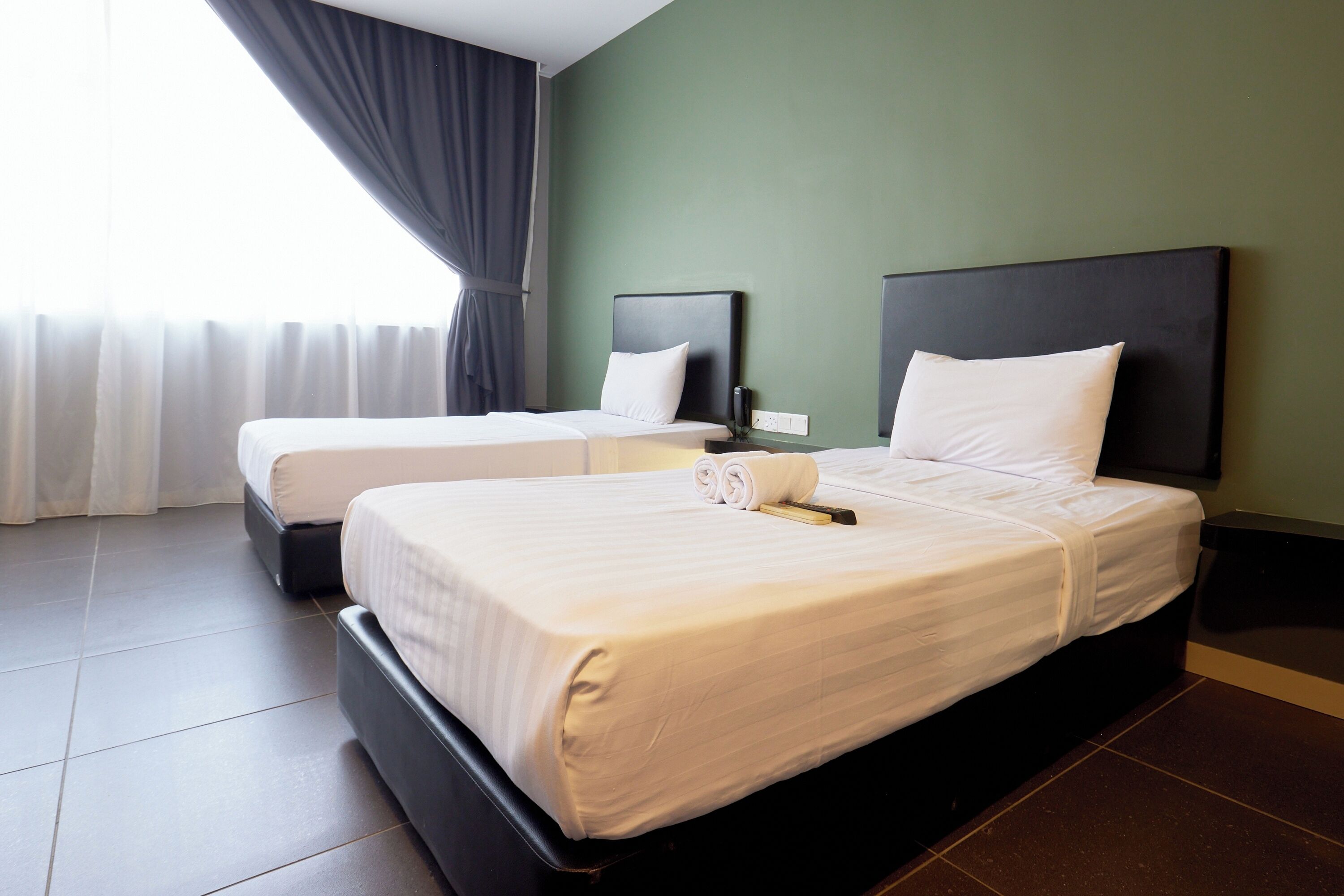 A hotel room with two beds, a flat-screen TV, and a large window with curtains.