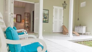 A covered porch with white chairs and a wicker chair, a white cabinet, and a painting on the wall. - Bungalow Sud (Koggala)