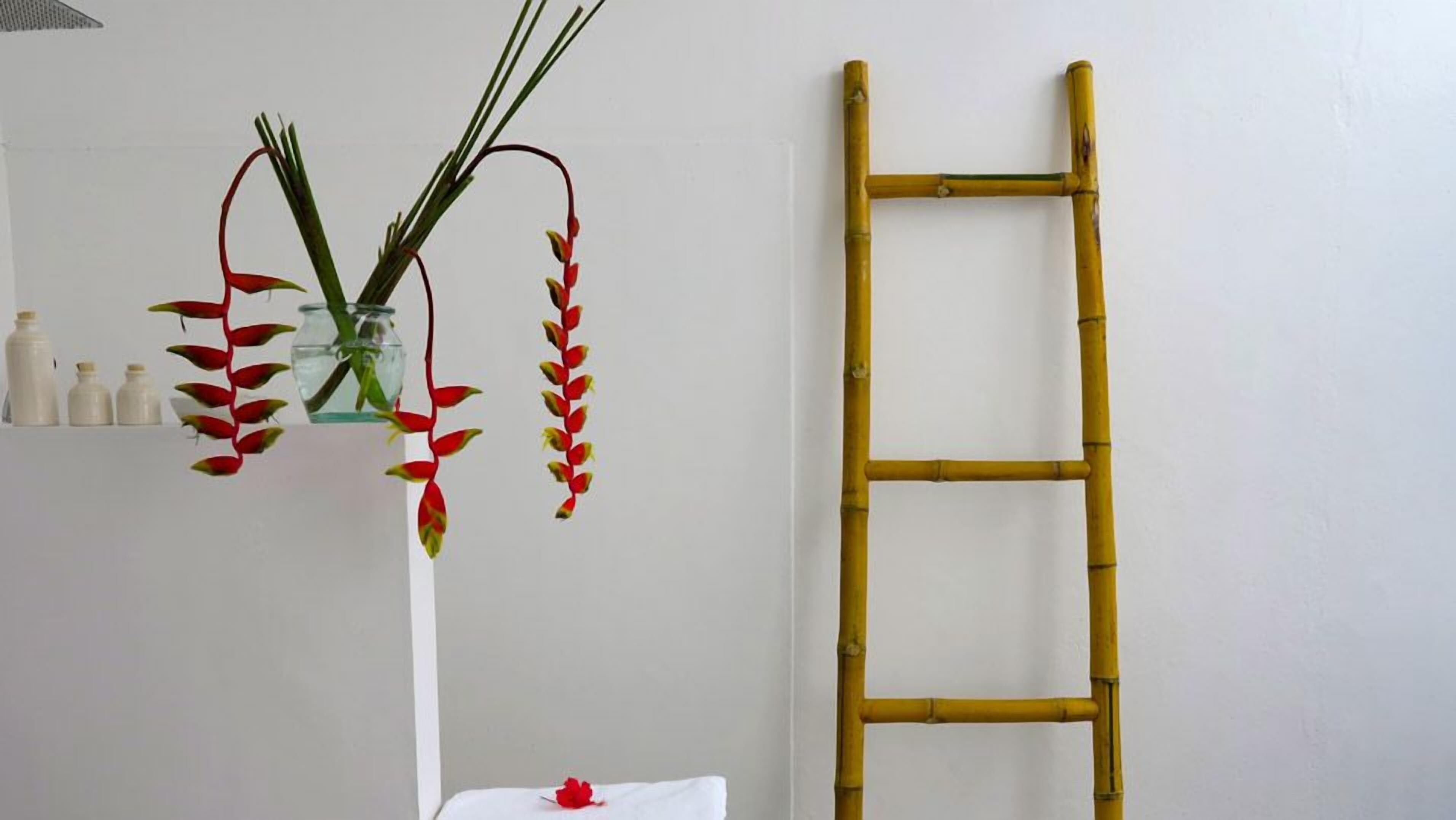 Een witte vaas met rode en groene bladeren, een bamboe ladder en kleine witte flesjes op een plank.