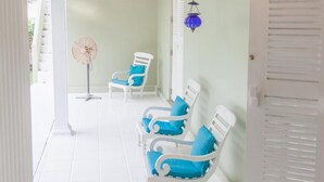 A covered porch with white chairs and a fan, a lantern, and a door. - Bungalow Sud (Koggala)