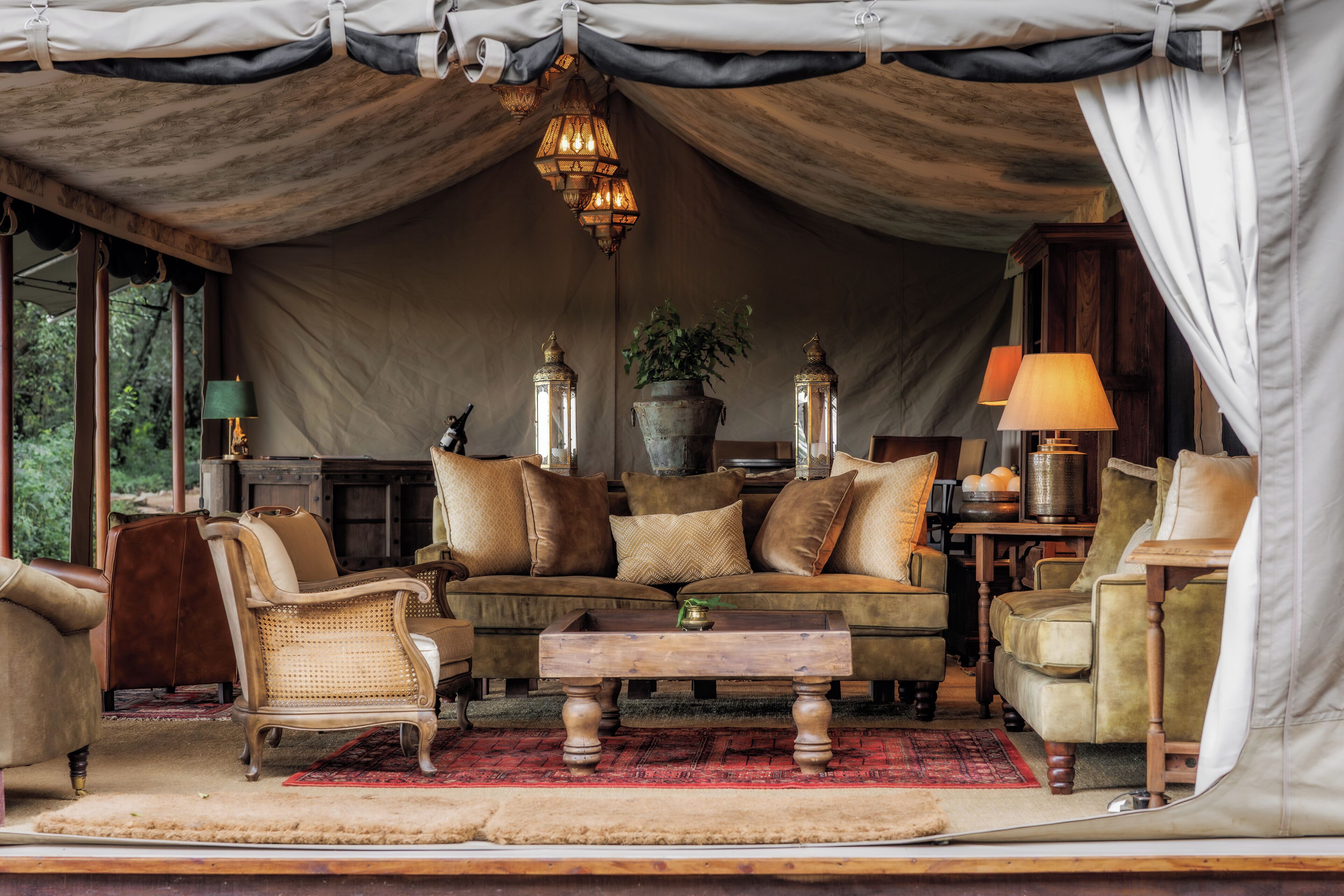 A tented room with a sofa, chairs, a coffee table, and a lamp.