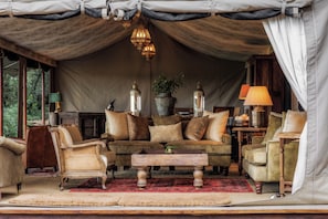 A tented room with a sofa, chairs, a coffee table, and a lamp. - Elewana Elephant Pepper Camp (Maasai Mara)