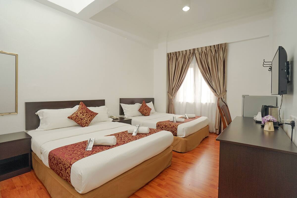 Quarto de hotel com duas camas, uma escrivaninha, televisão e janela com cortinas.
