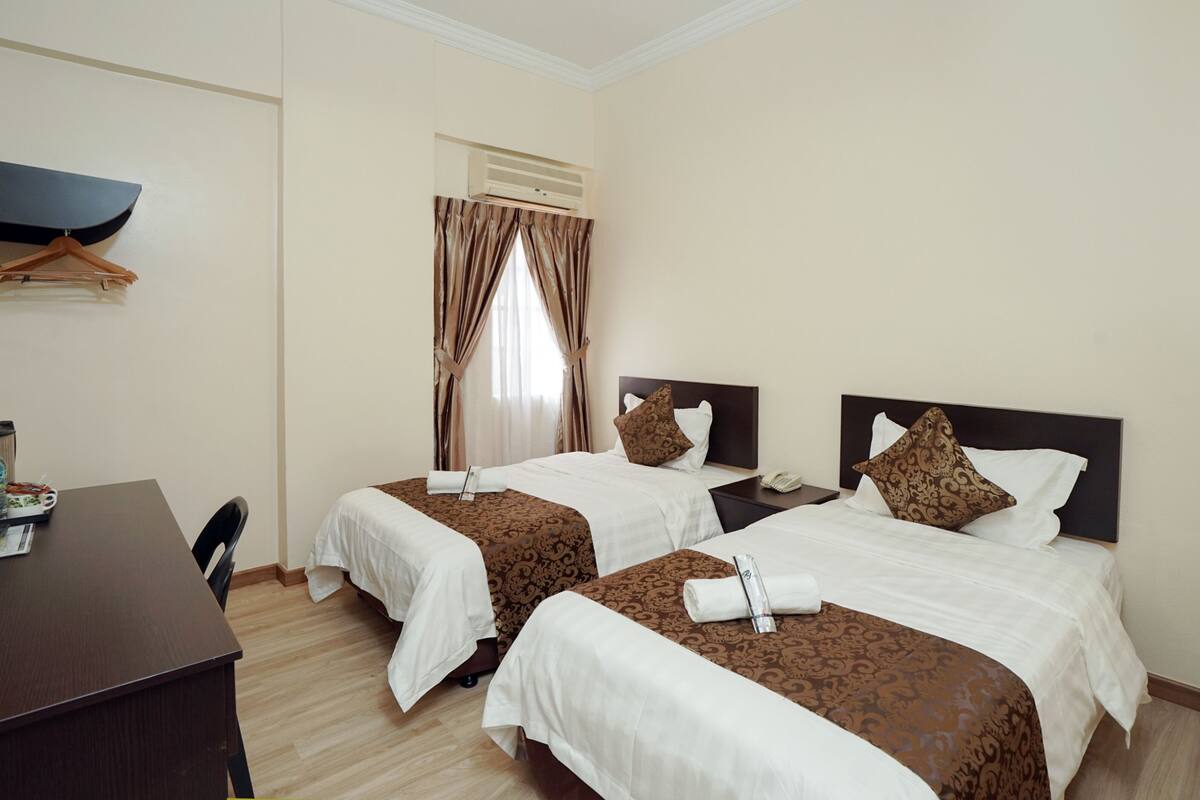 Quarto de hotel com duas camas, uma escrivaninha e uma cadeira.