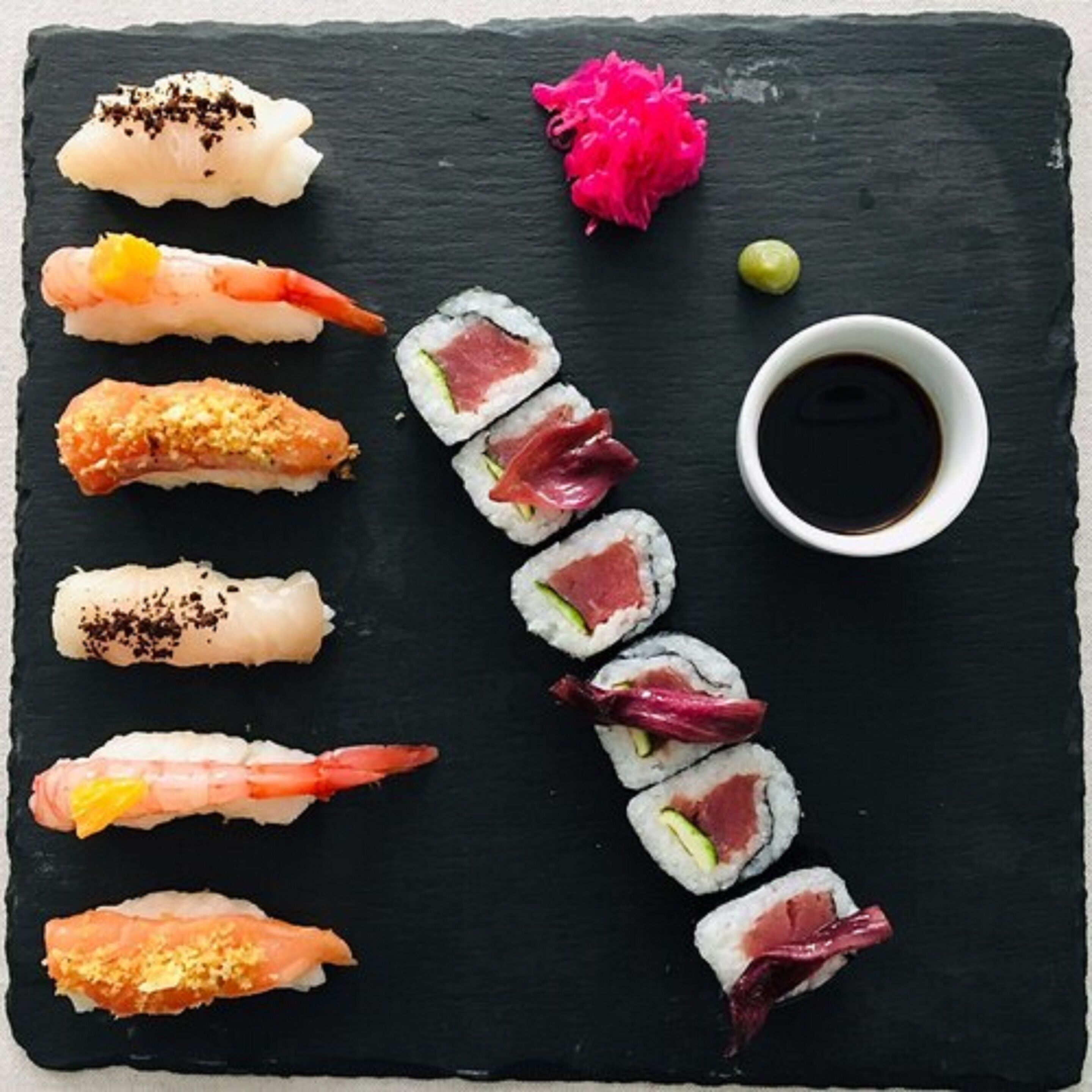 A variety of sushi arranged on a black slate board.