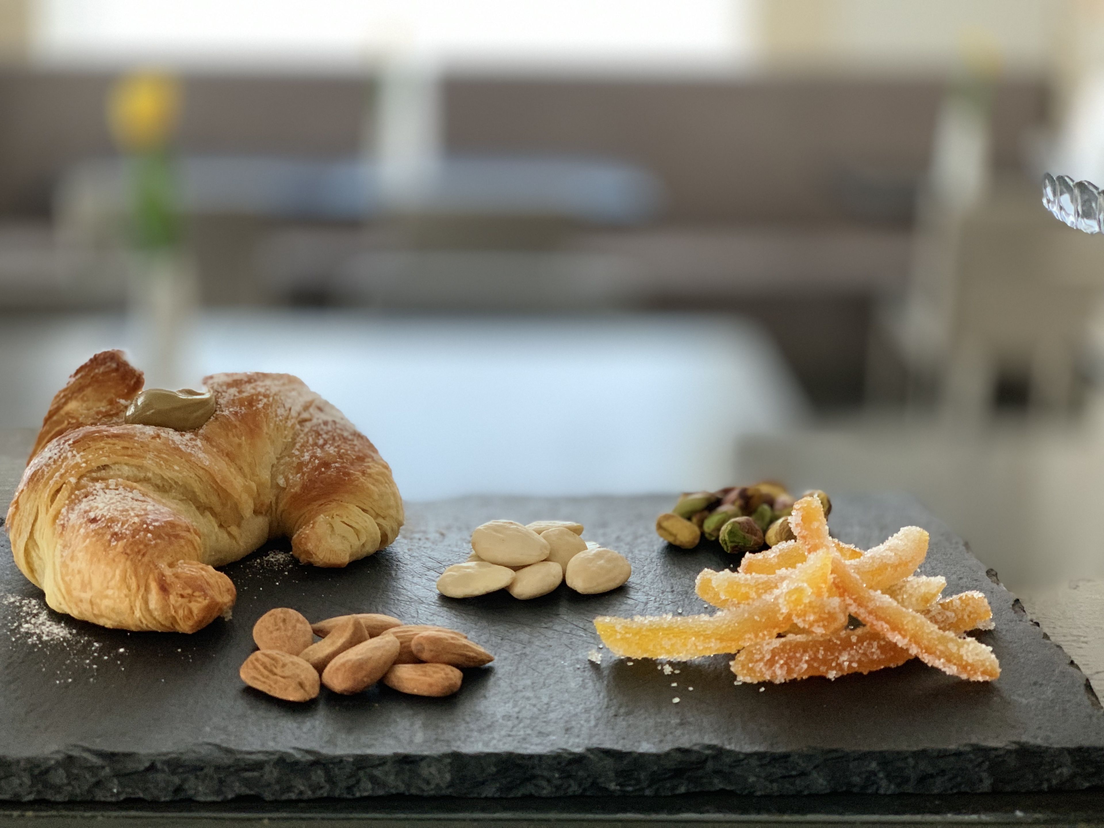 A croissant with almonds and sugar-coated almonds on a slate board.