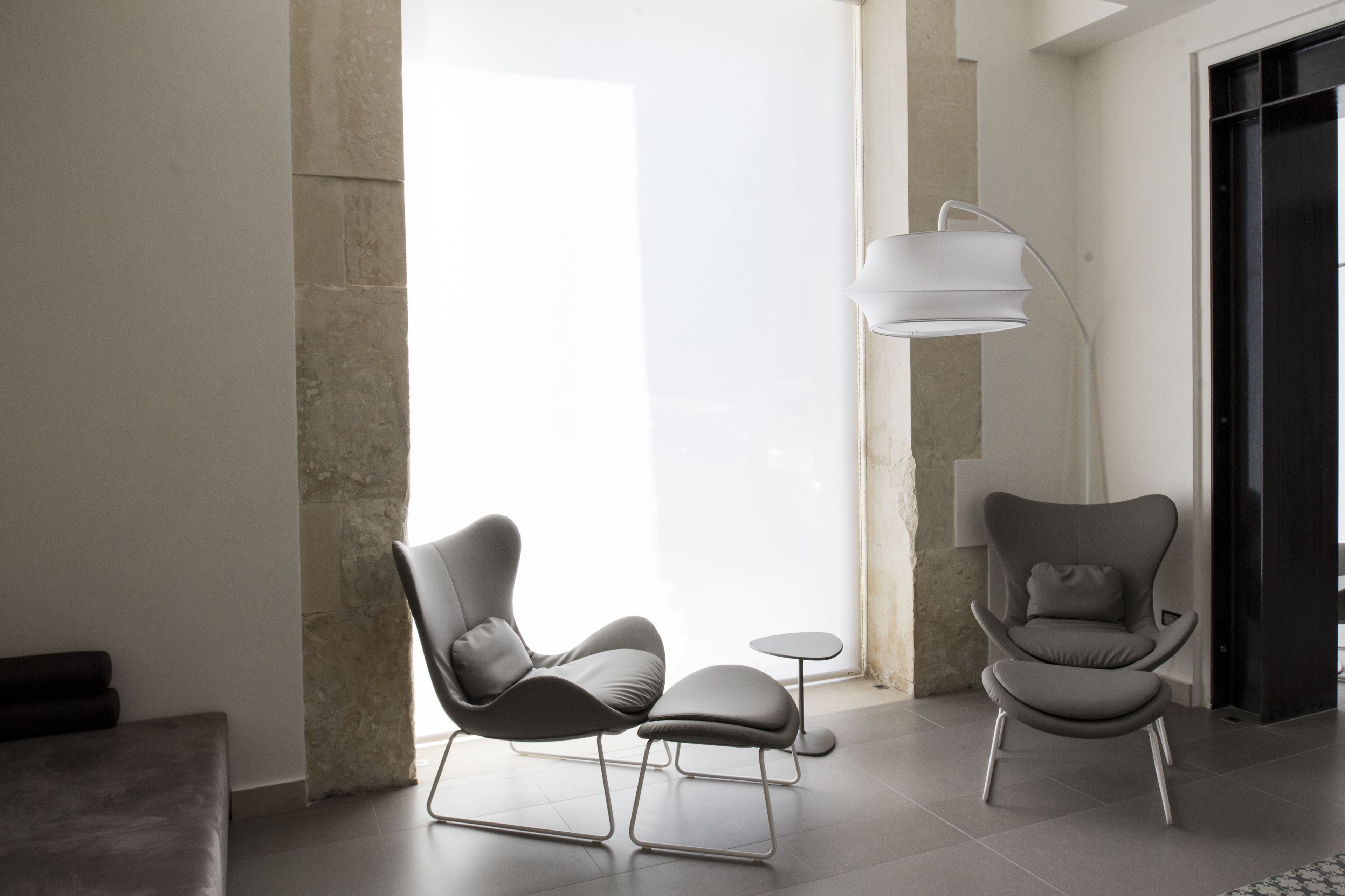 Un intérieur moderne avec deux chaises contemporaines et une petite table, un lampadaire et une grande fenêtre qui laisse entrer la lumière naturelle.