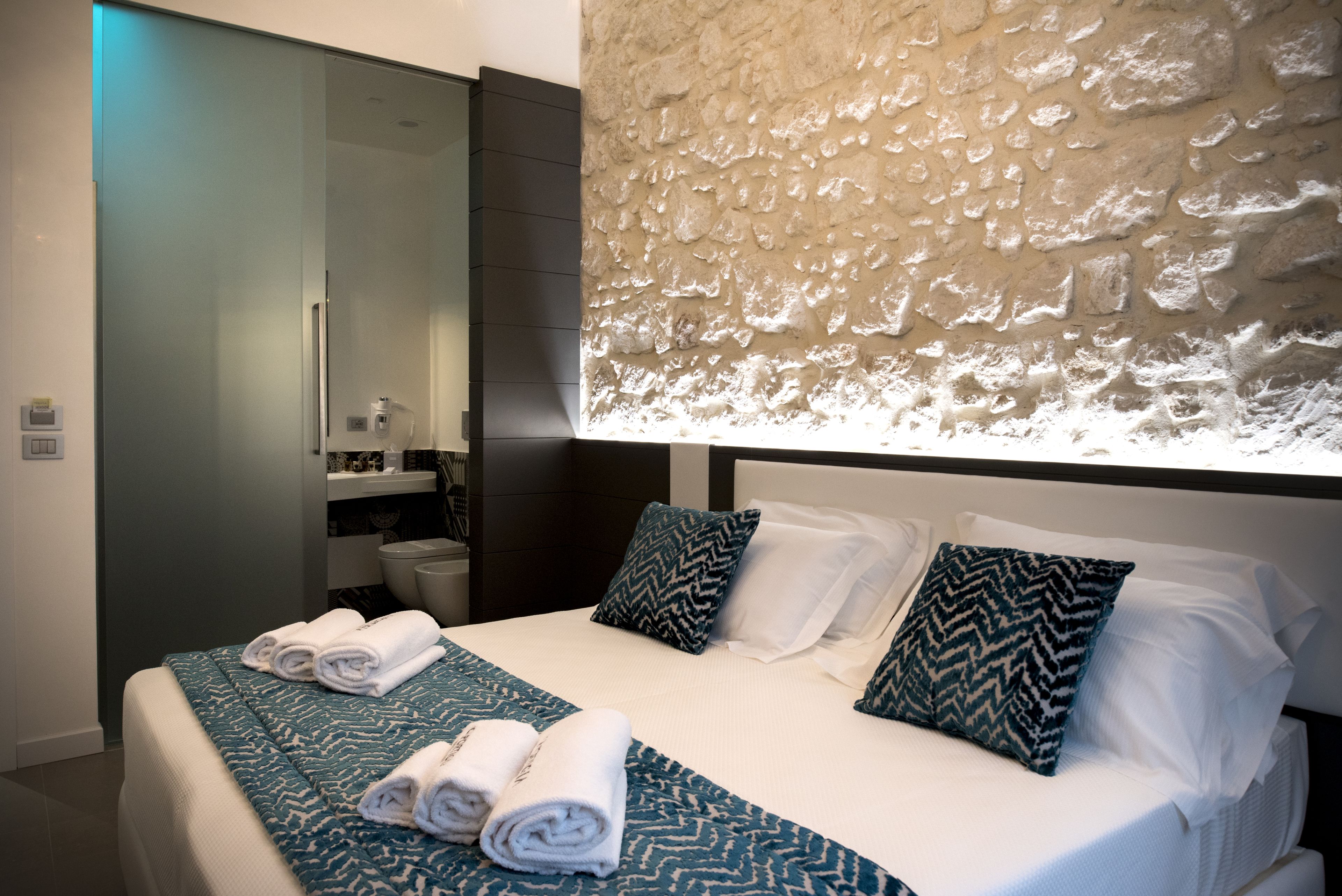 A modern hotel room with a large bed, a bathroom with a mirror, and a textured wall.