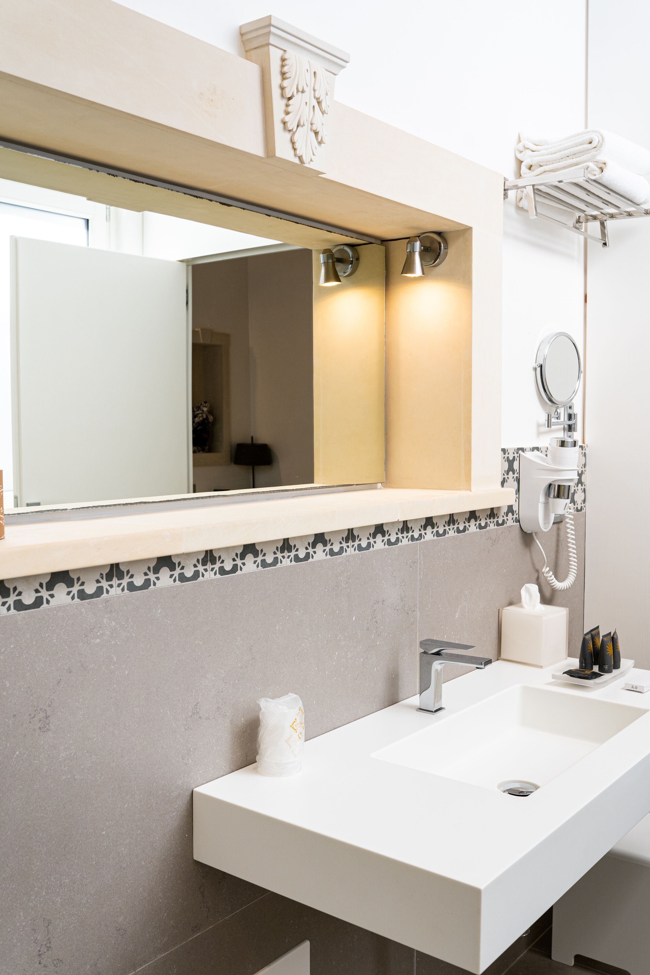 A modern bathroom with a large mirror, a white sink, and a towel rack.