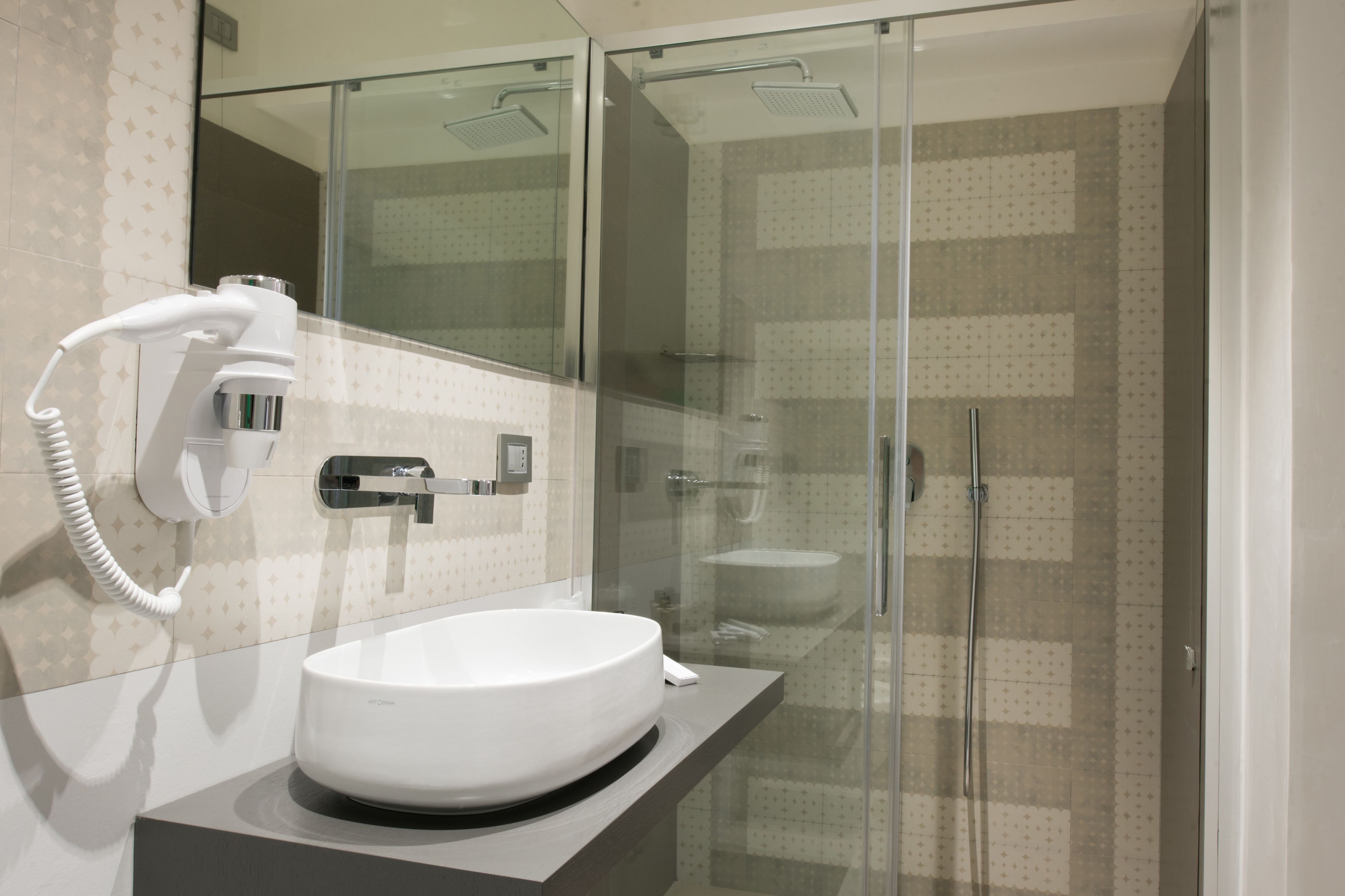 Un baño moderno con ducha de vidrio, lavamanos blanco y un secador de pelo en la pared.