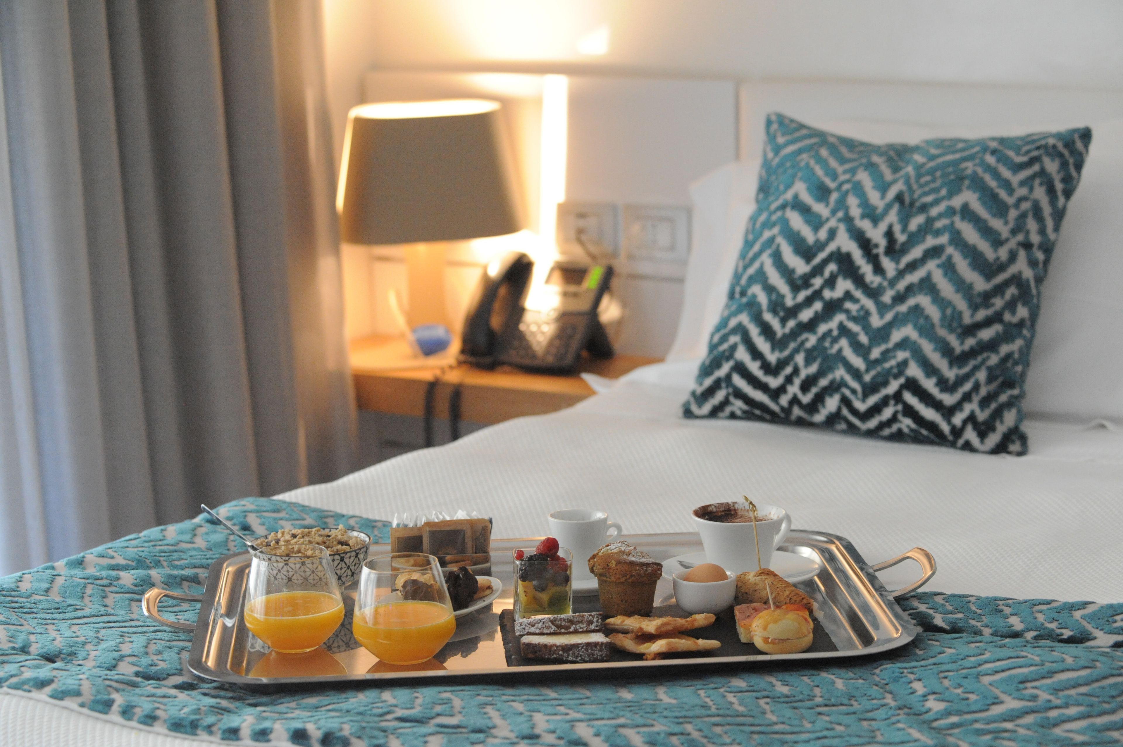 Bandeja de desayuno con diferentes elementos sobre una cama en una habitación de hotel.