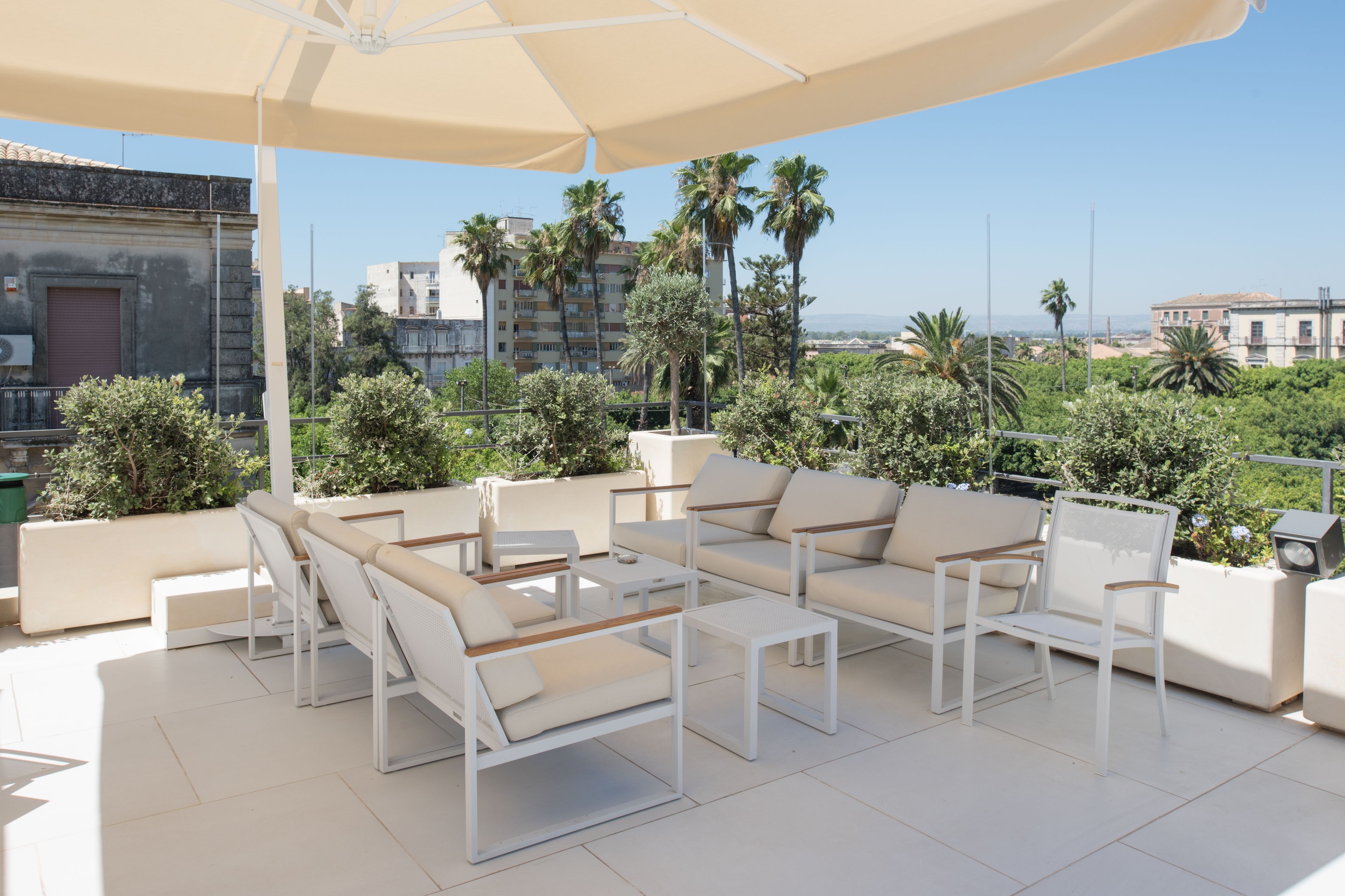 Una terraza en la azotea con mobiliario blanco, incluyendo sofás y sillones, bajo un gran toldo.
